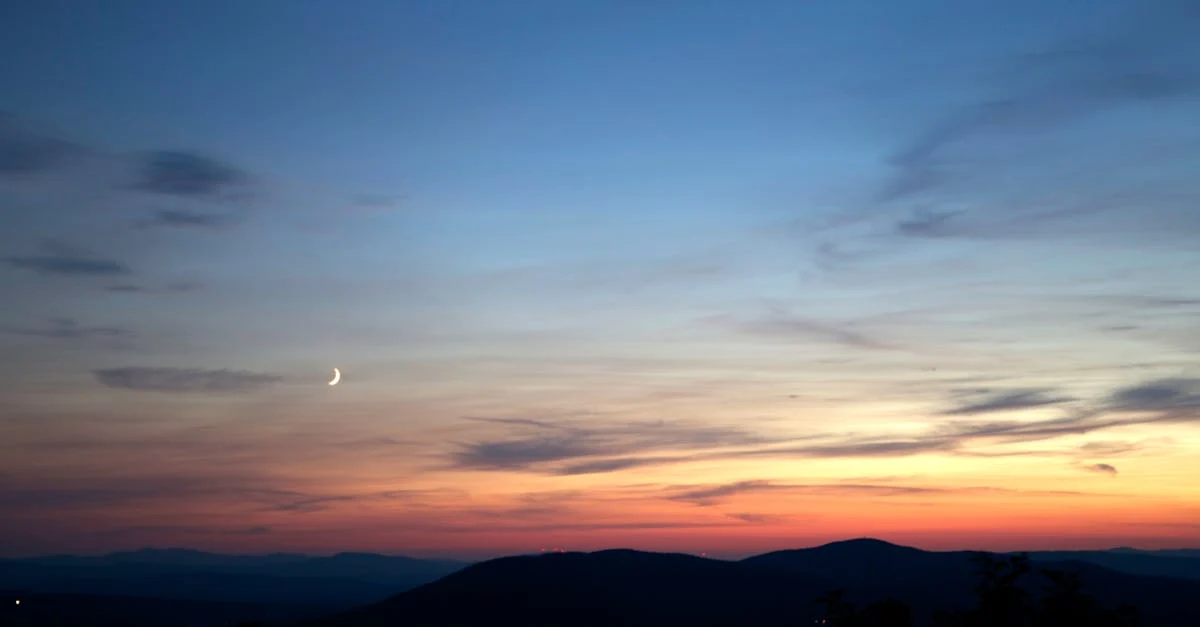 A serene dusk landscape with a crescent moon rising above softly layered hills, stars emerging in a deep twilight sky